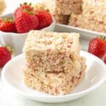 Two strawberry rice crispy treats stacked on top of each other, they sit on a small plate.