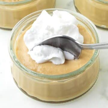 A spoon scooping out a spoonful of butterscotch pudding and coconut whipped cream from a small bowl.