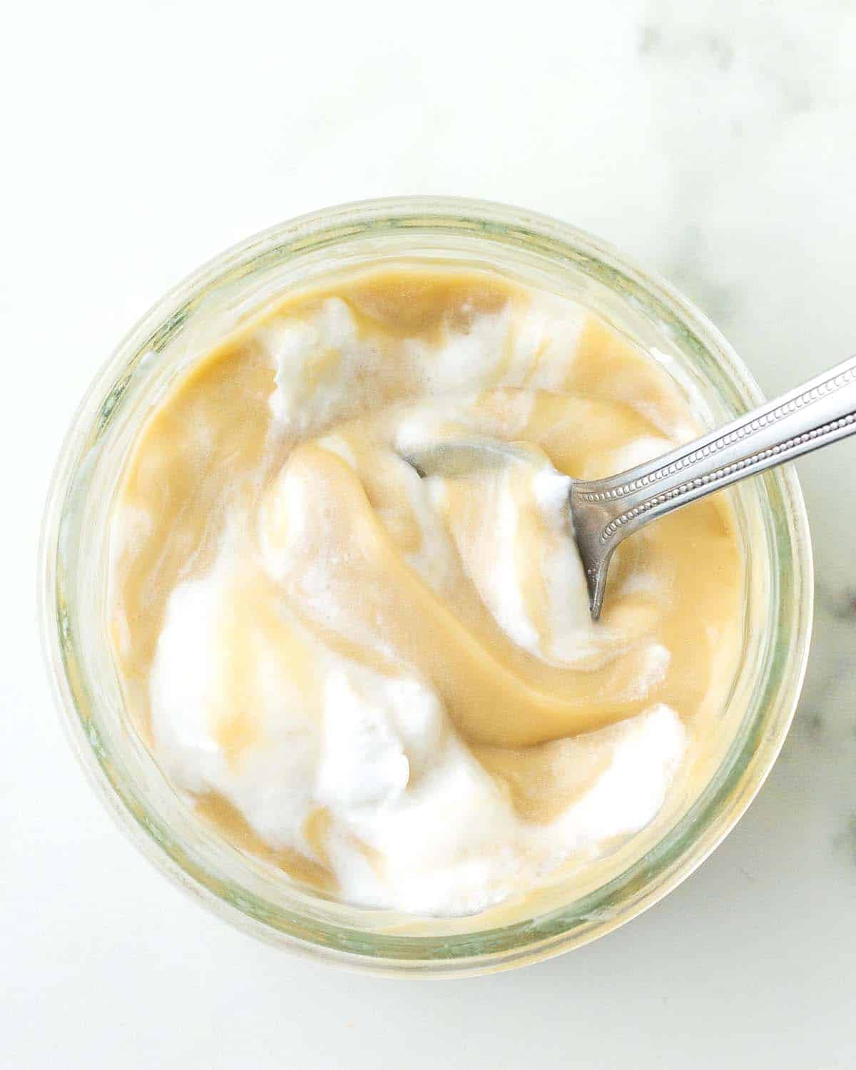 An overhead shot of a bowl of butterscotch pudding and whipped cream with a spoon in it.