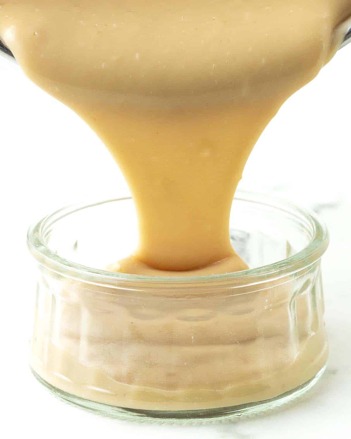 Homemade vegan butterscotch pudding being poured from a pot into a glass bowl.