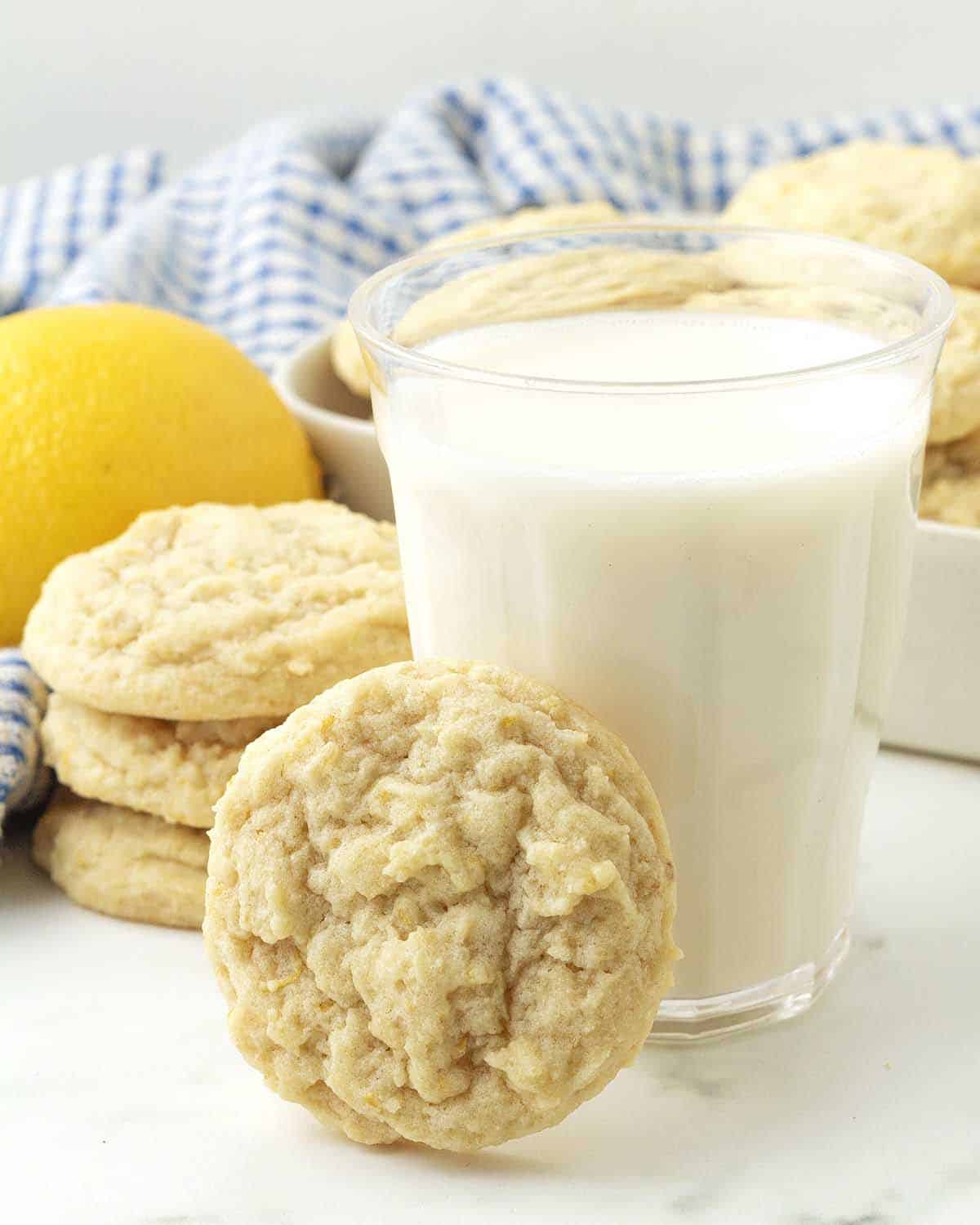 A lemon cookie leaning against a glass of almond milk.