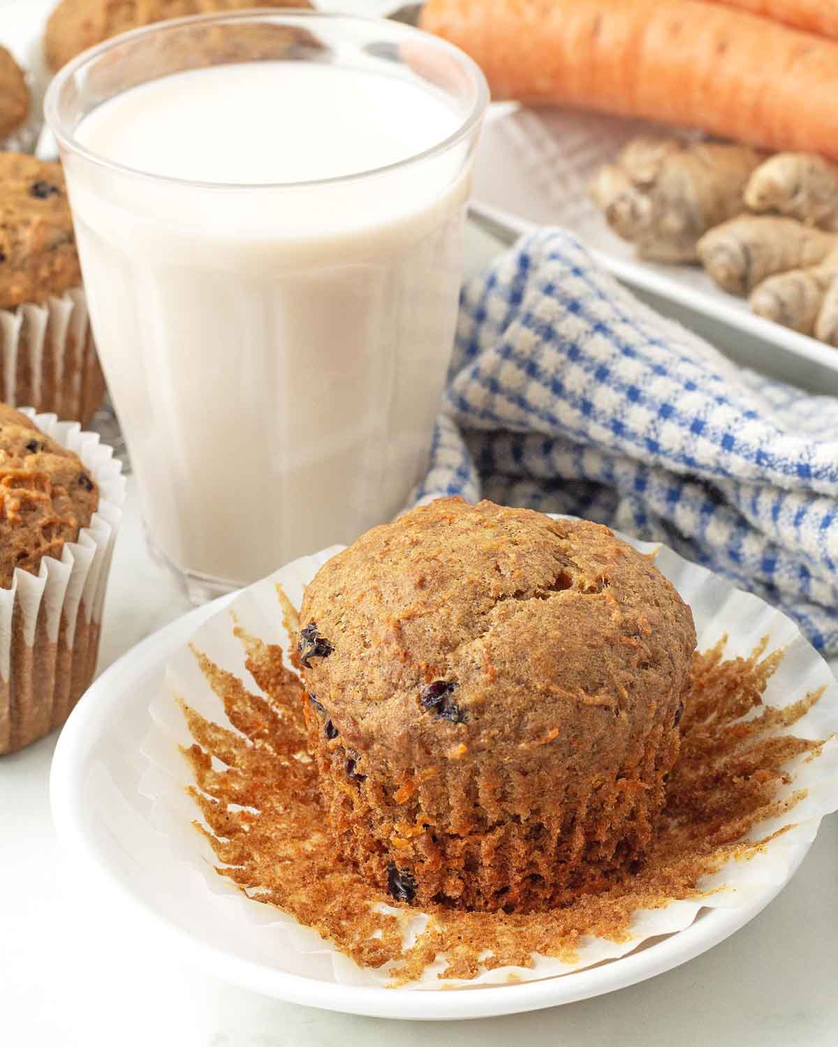 A carrot ginger muffin on a plate, the muffin wrapper has been peeled away.