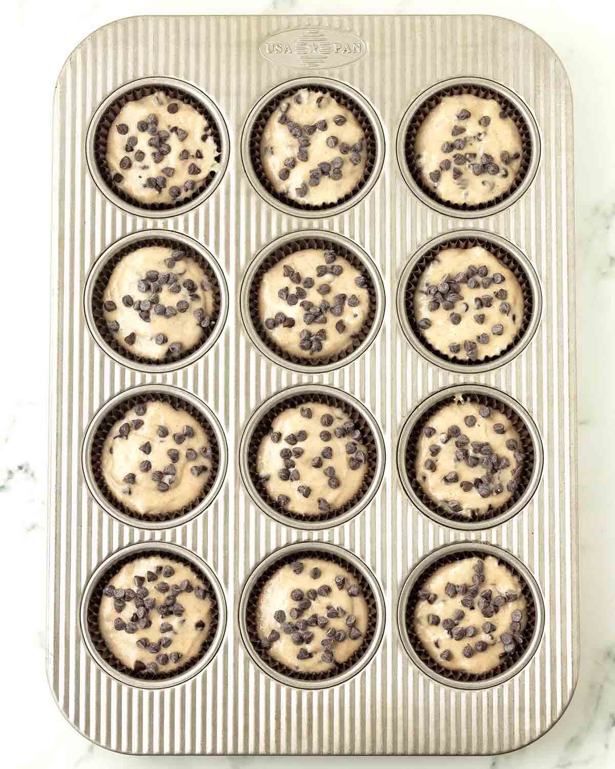 An overhead image of vegan chocolate chip muffin batter in a muffin pan about to be baked.