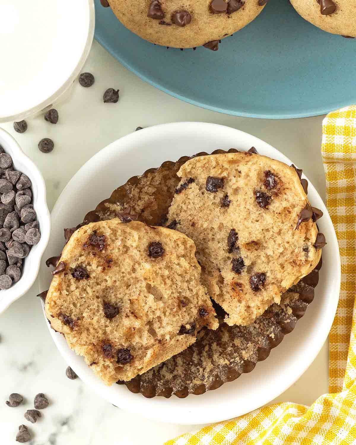 A chocolate chip muffin on a small plate, the muffin has been split in half to show the fluffy interior.