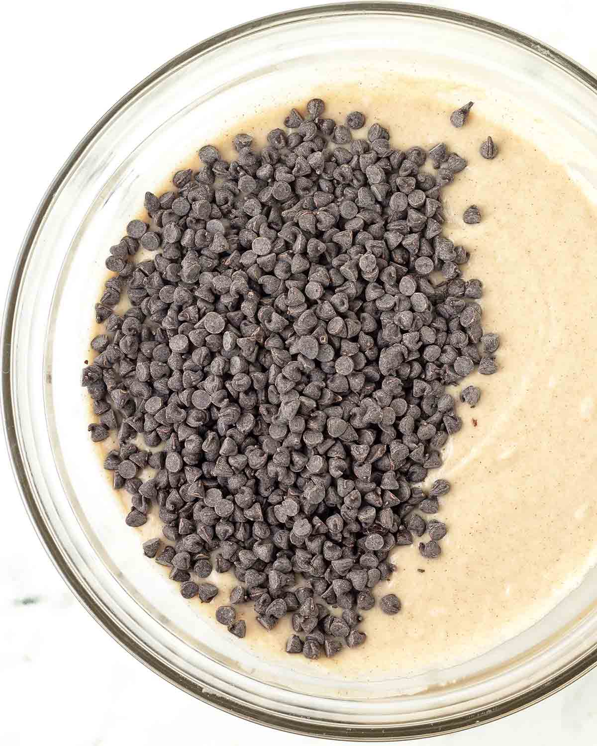 A bowl with muffin batter, chocolate chips sit on top of the batter waiting to be mixed in.