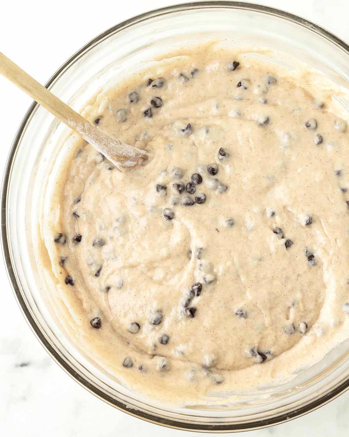 The mixed muffin batter for chocolate chip muffins and a wooden spoon in a glass bowl.
