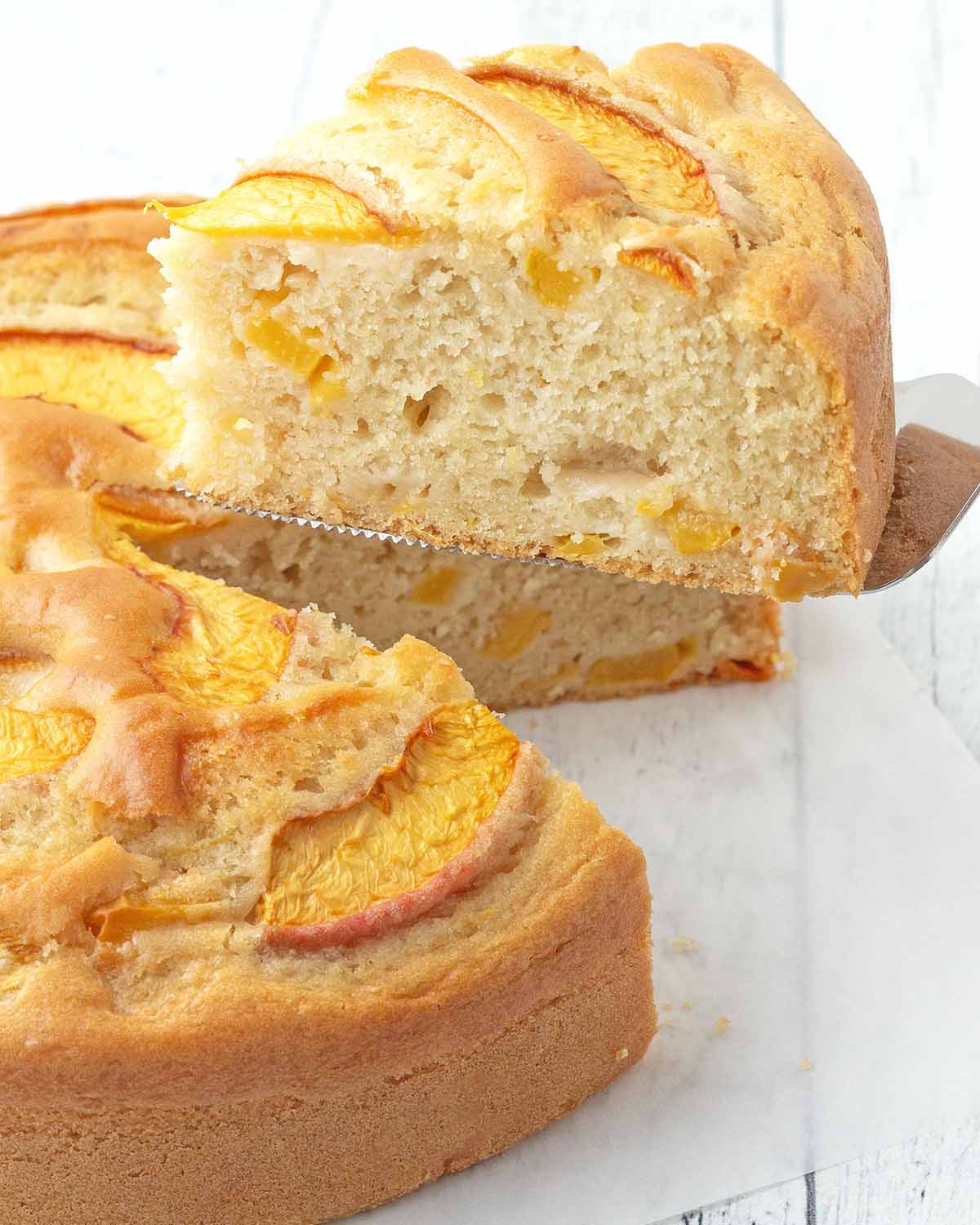 A slice of vegan peach cake cake being held on a cake server.