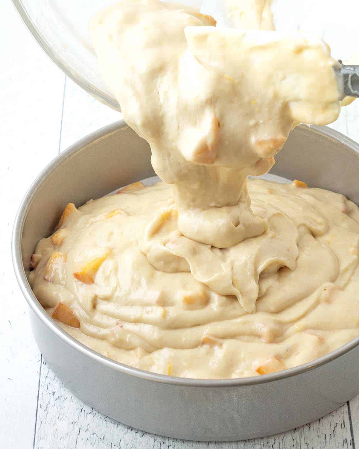 Peach cake batter being poured from a bowl into a cake pan.