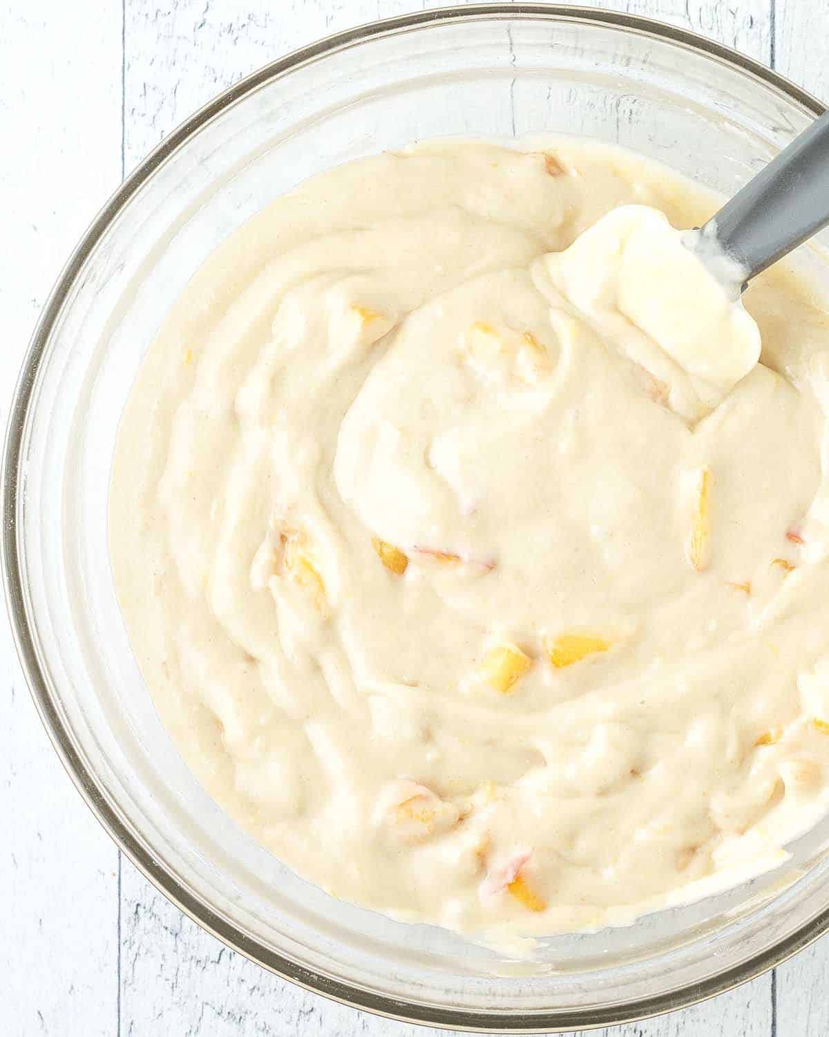 Peach cake batter and a rubber spatula in a glass bowl.