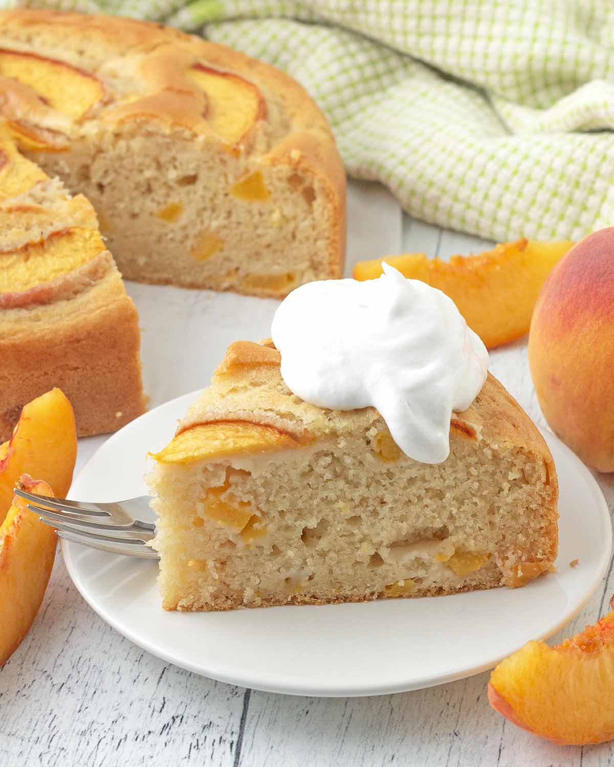 A slice of peach cake on a white plate with whipped cream on top.