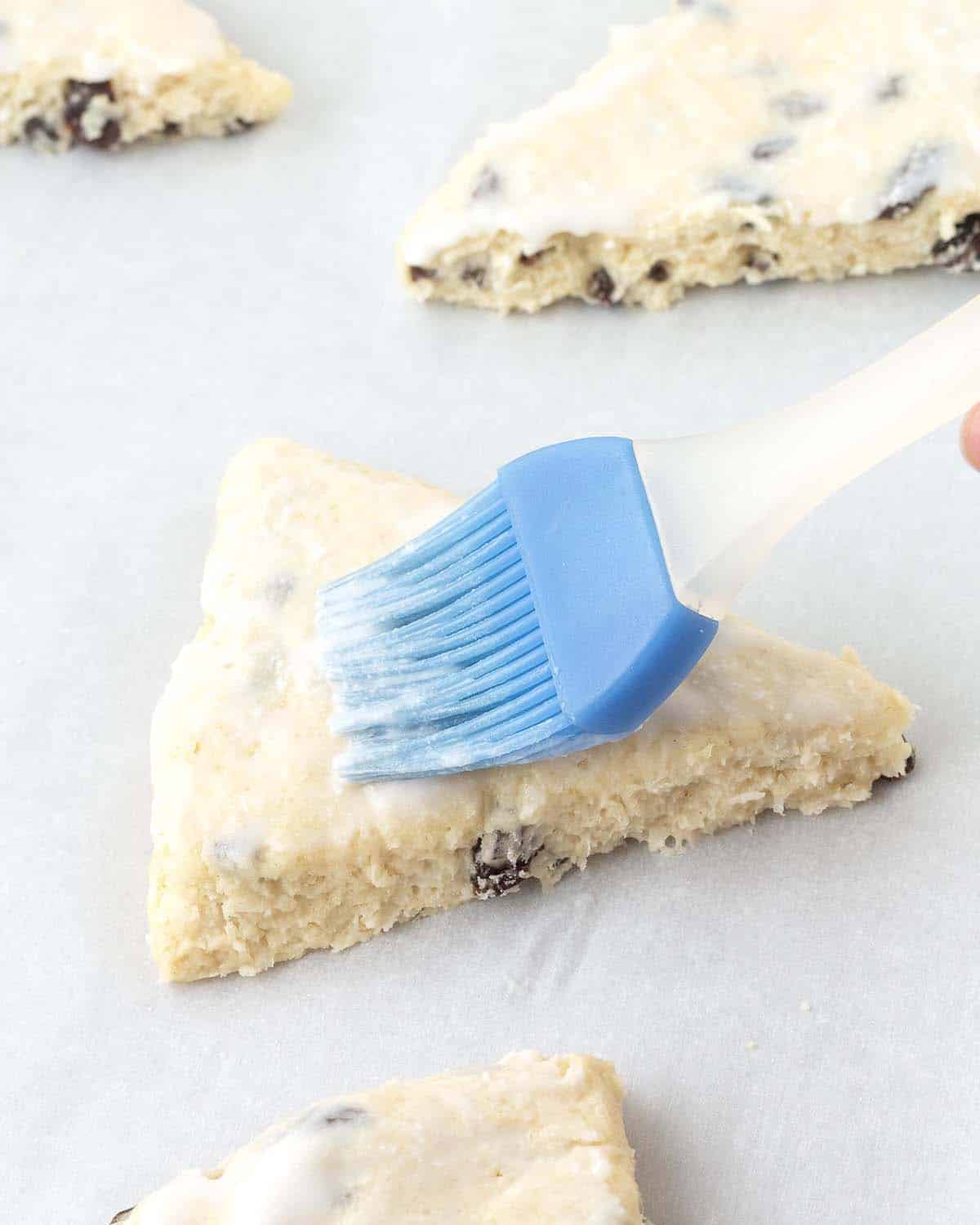A pastry brush brushing coconut milk onto the top of an unbaked scone.