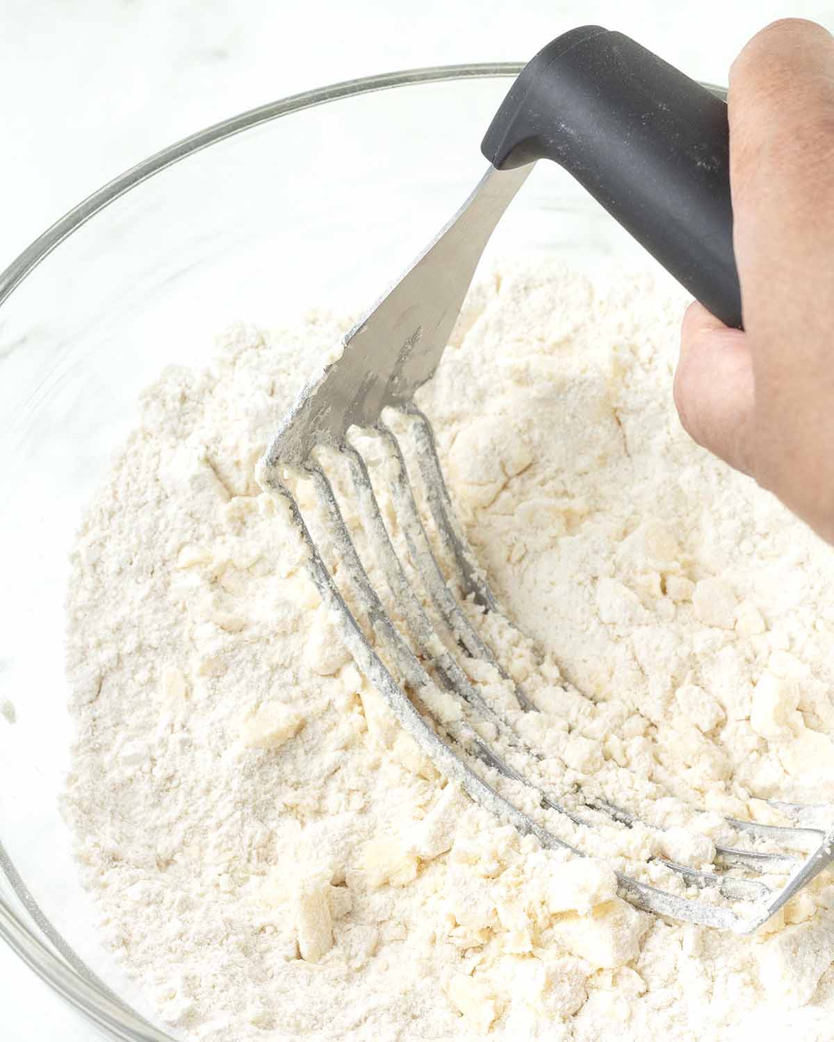 A hand cutting butter into flour using a pastry cutter.
