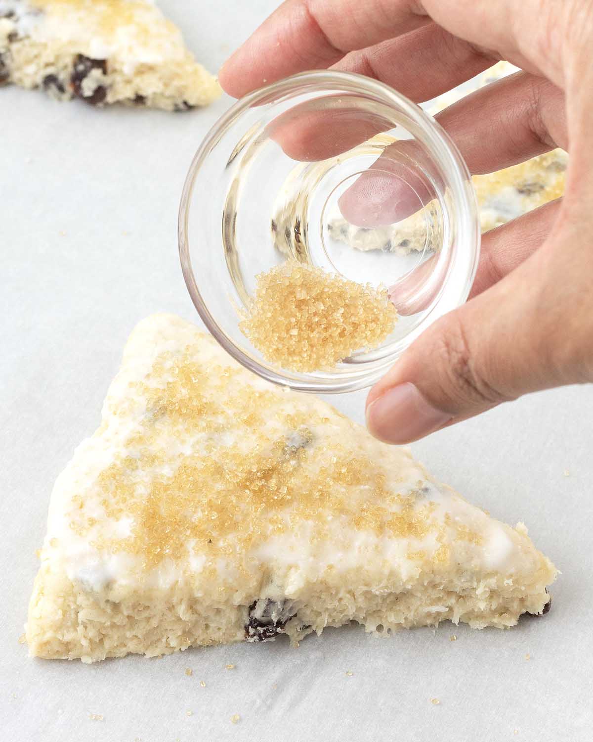 A hand sprinkling sugar on top of unbaked scones.