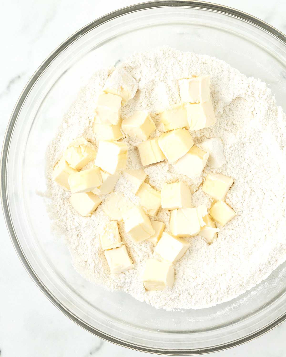 A bowl with flour, cubed butter sits on top of the flour.