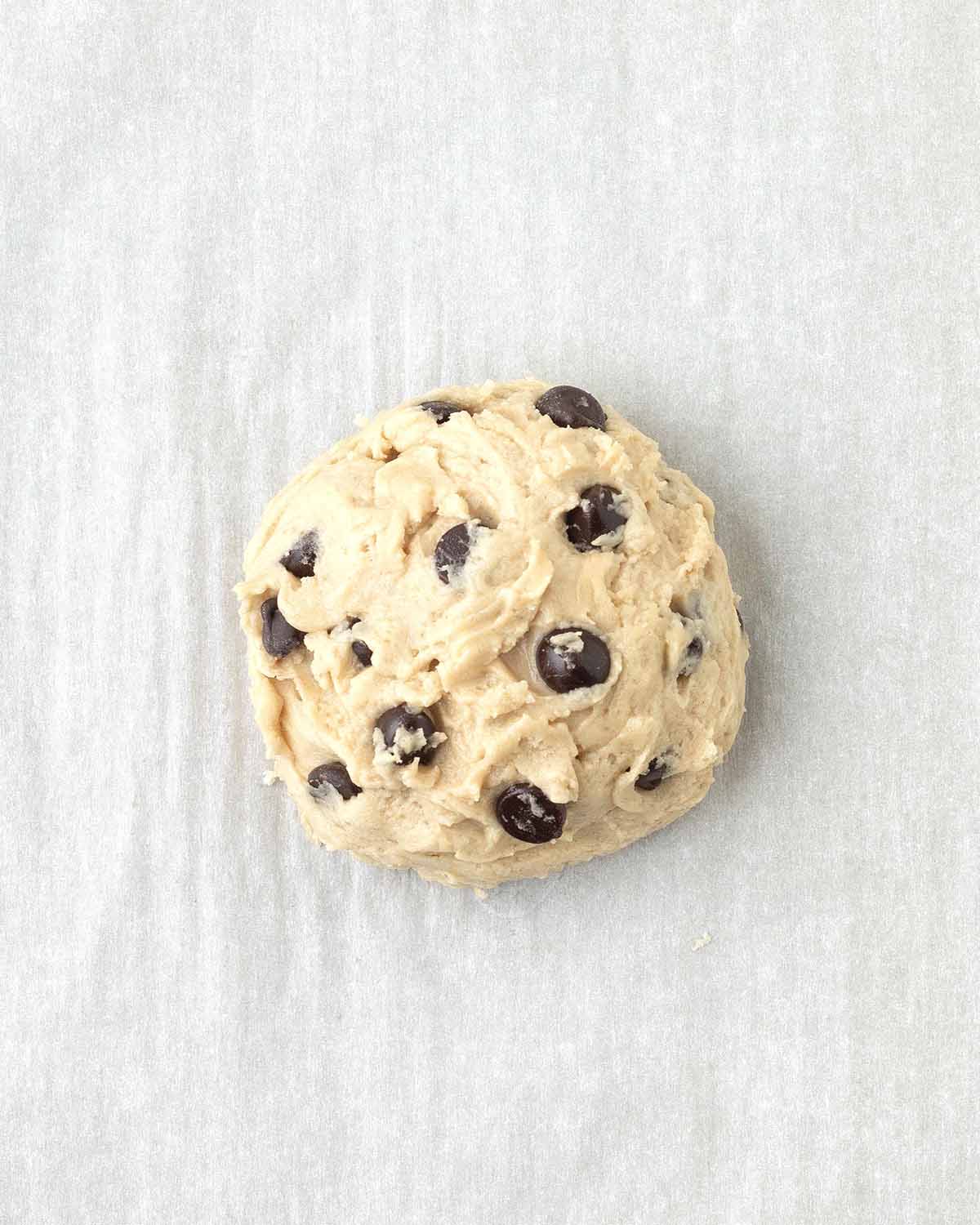 A ball of unbaked cookie dough on a parchment lined baking sheet.