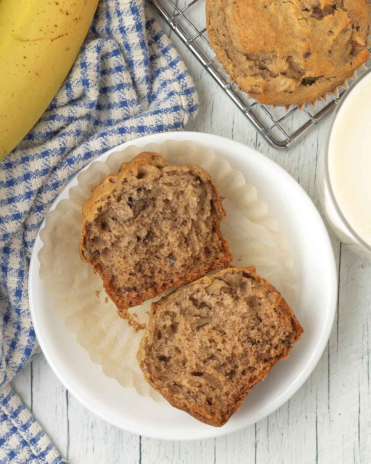 A banana muffin on a small plate, the muffin has been split in half to show the fluffy interior.