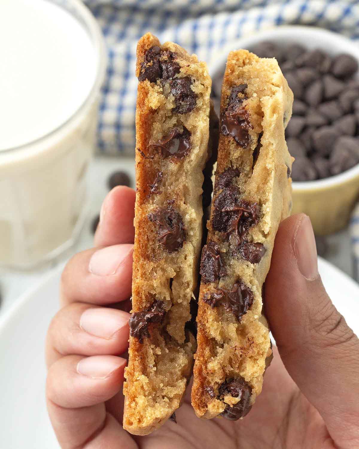 A hand holding a split cookie showing the soft, gooey inside.