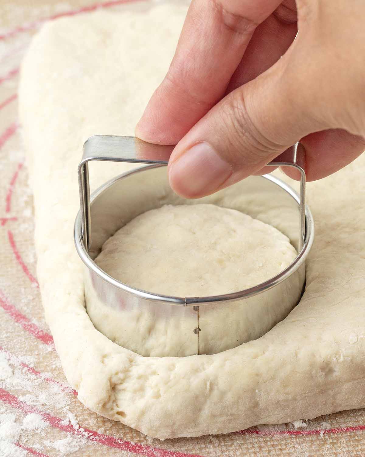 A hand pressing a circle metal biscuit cutter into biscuit dough.