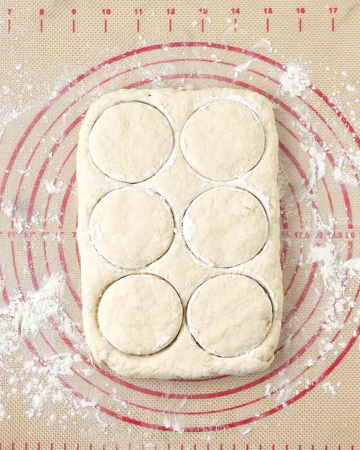 Biscuit dough that has six circle cutouts waiting to be pulled away.