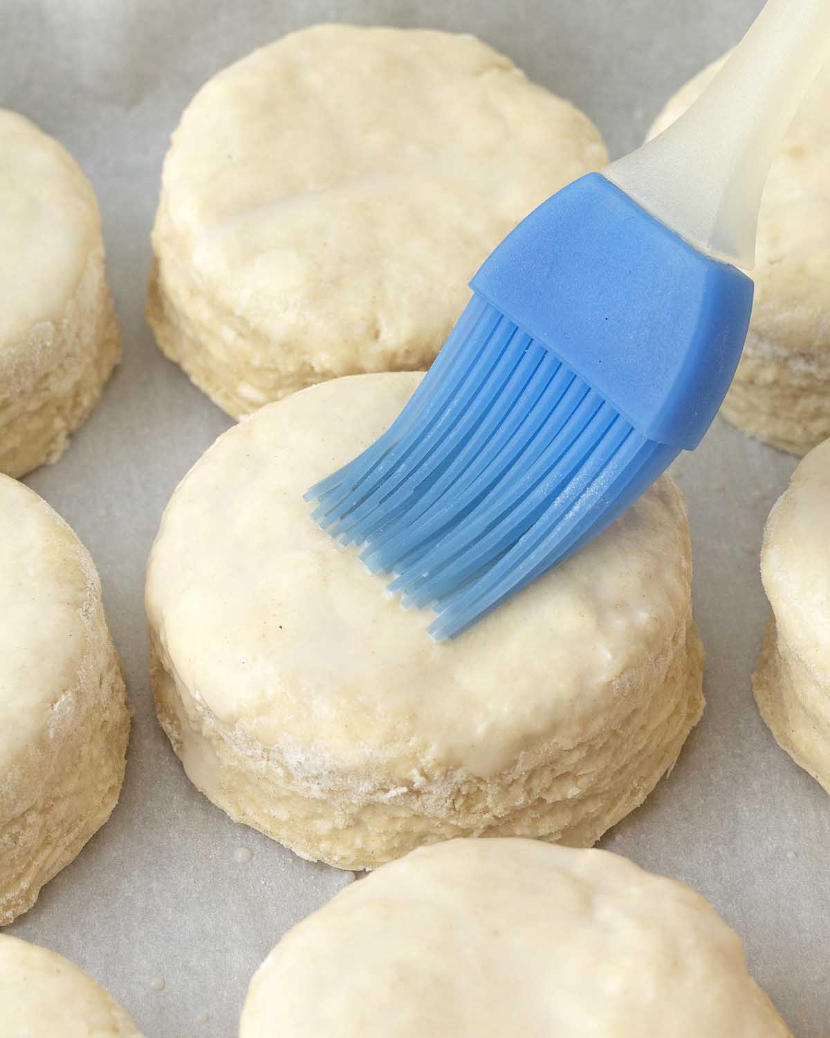 A pastry brush brushing dairy-free milk onto the top of an unbaked biscuit.
