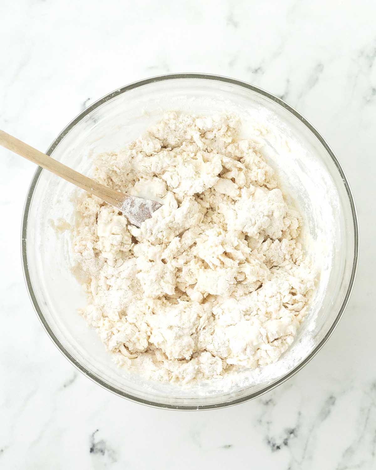 Biscuit dough in a glass bowl being mixed with a wooden spoon.