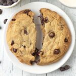 An overhead image of a large cookie on a white plate, the cookie has been split in half.
