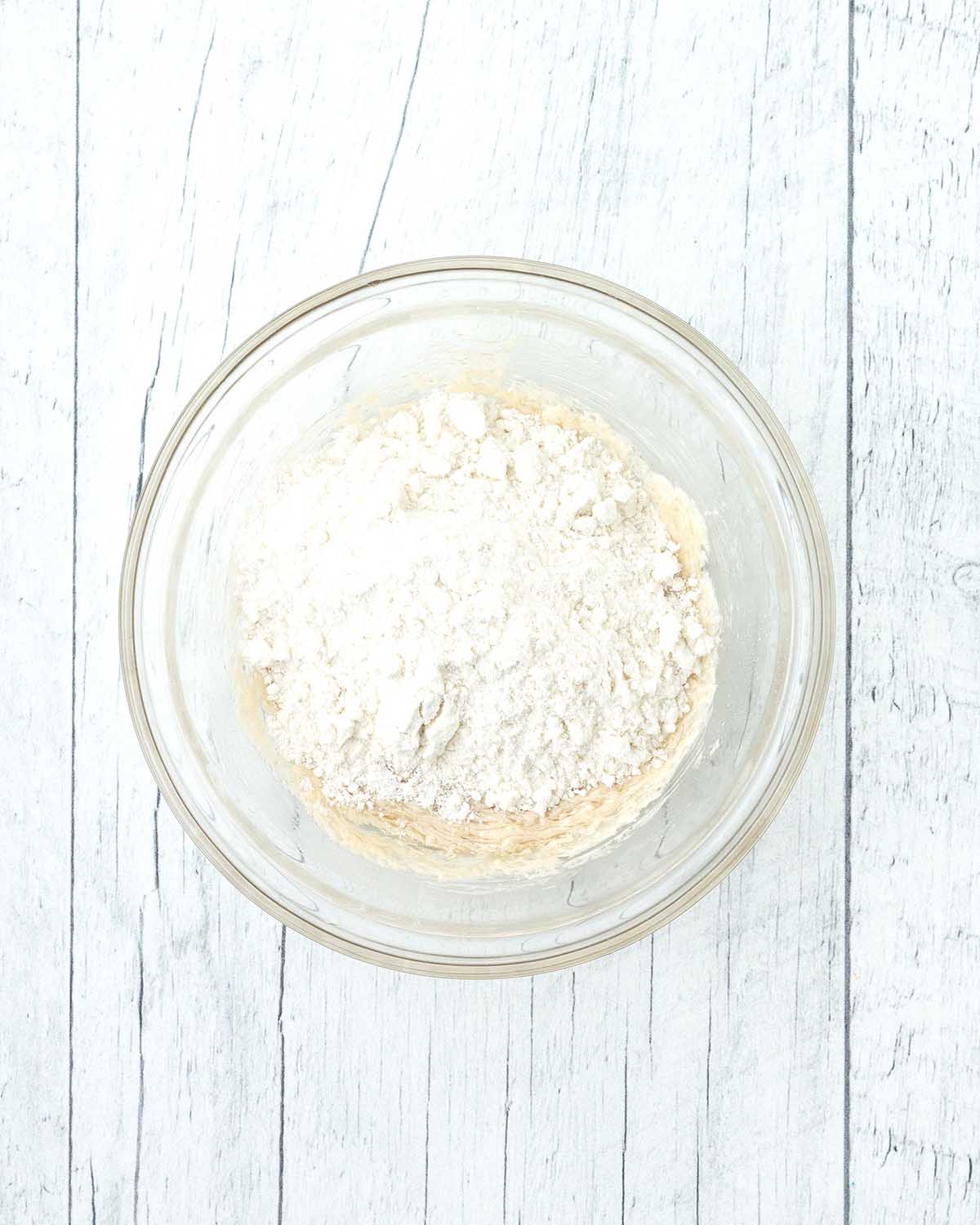 Cookie dough in a bowl, a flour mixture sits on top of the dough waiting to be mixed in.