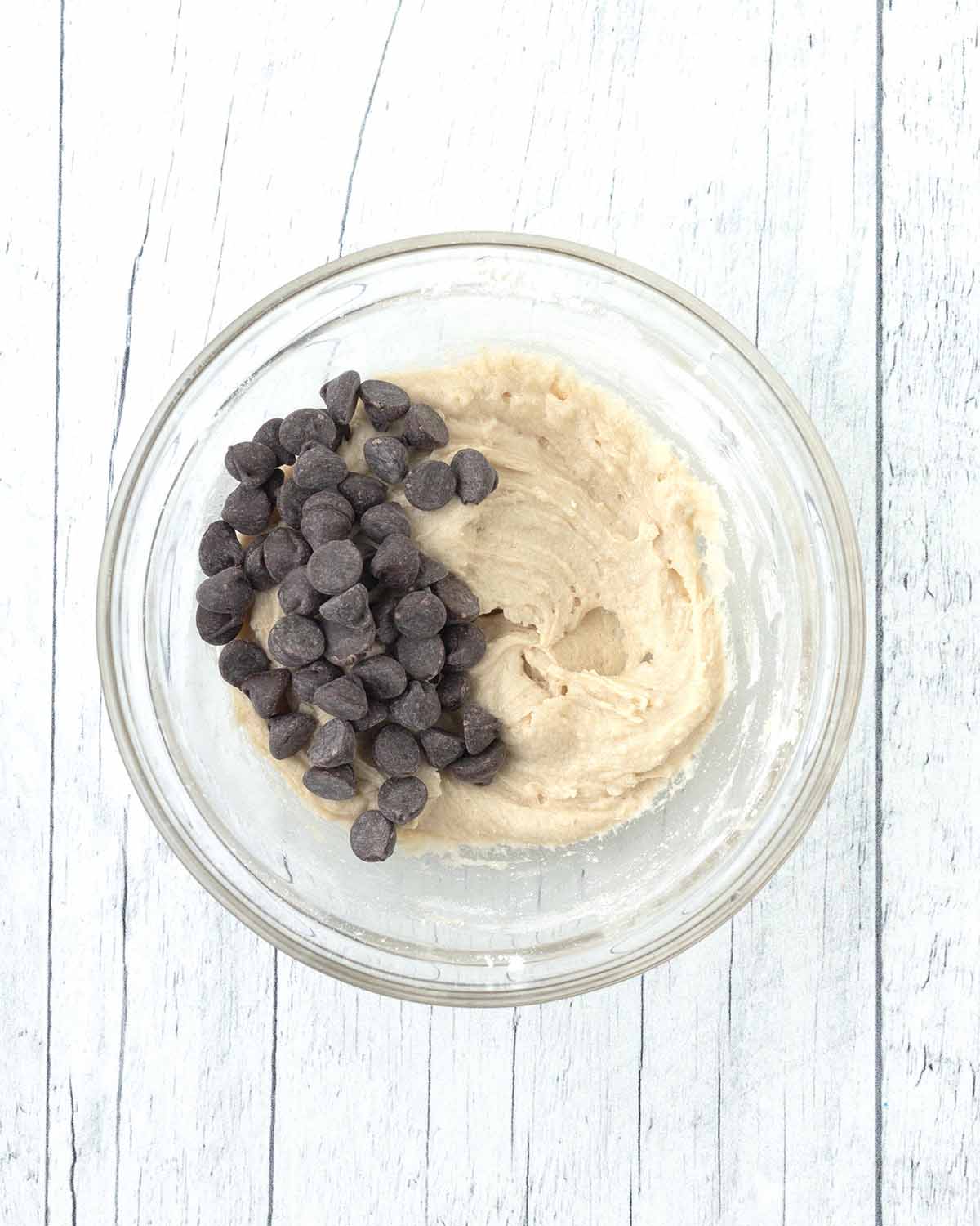 Cookie dough in a bowl, chocolate chips sit on top of the cookie dough.
