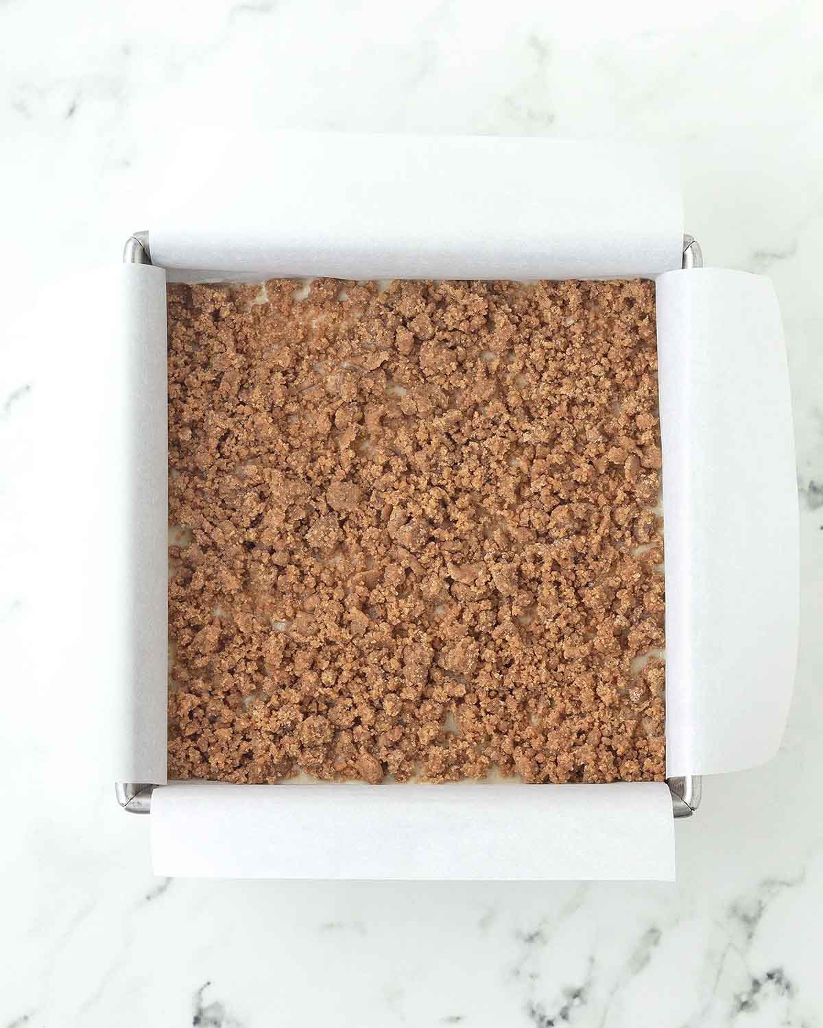 The middle layer of coffee cake cinnamon crumb on top of a layer of batter in a square pan.