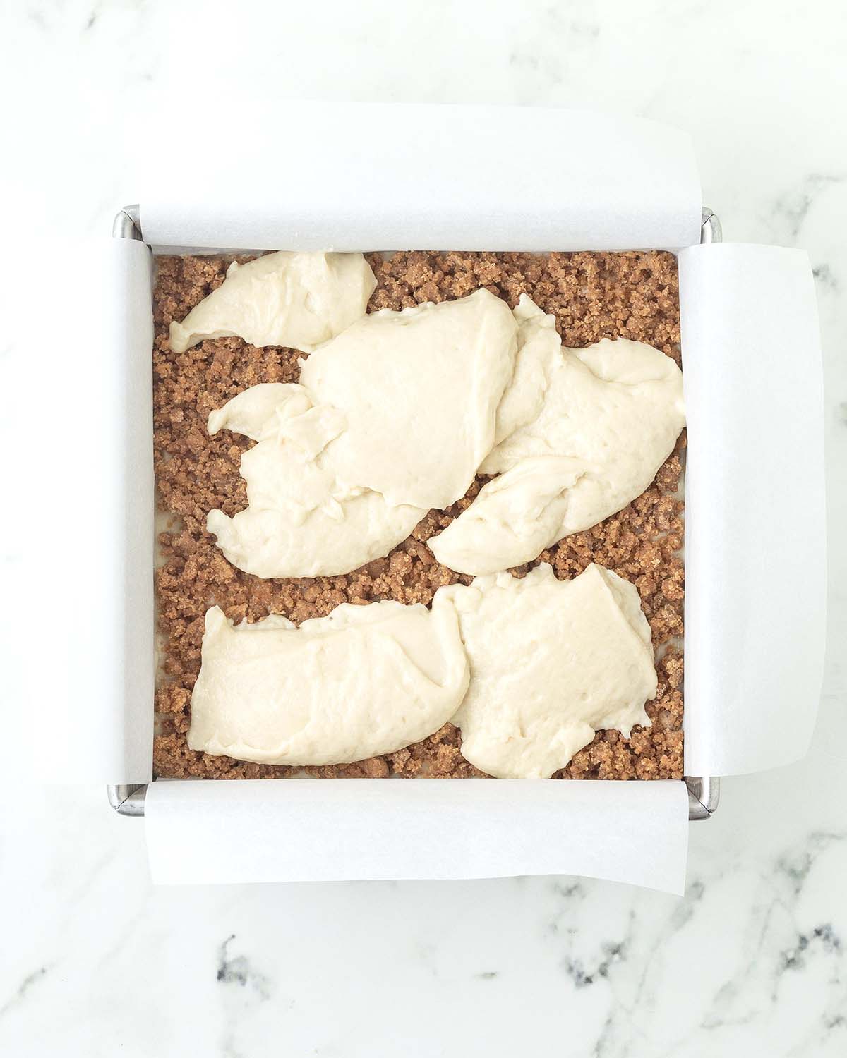 Dollops of batter on top of cinnamon crumb in a square baking pan.