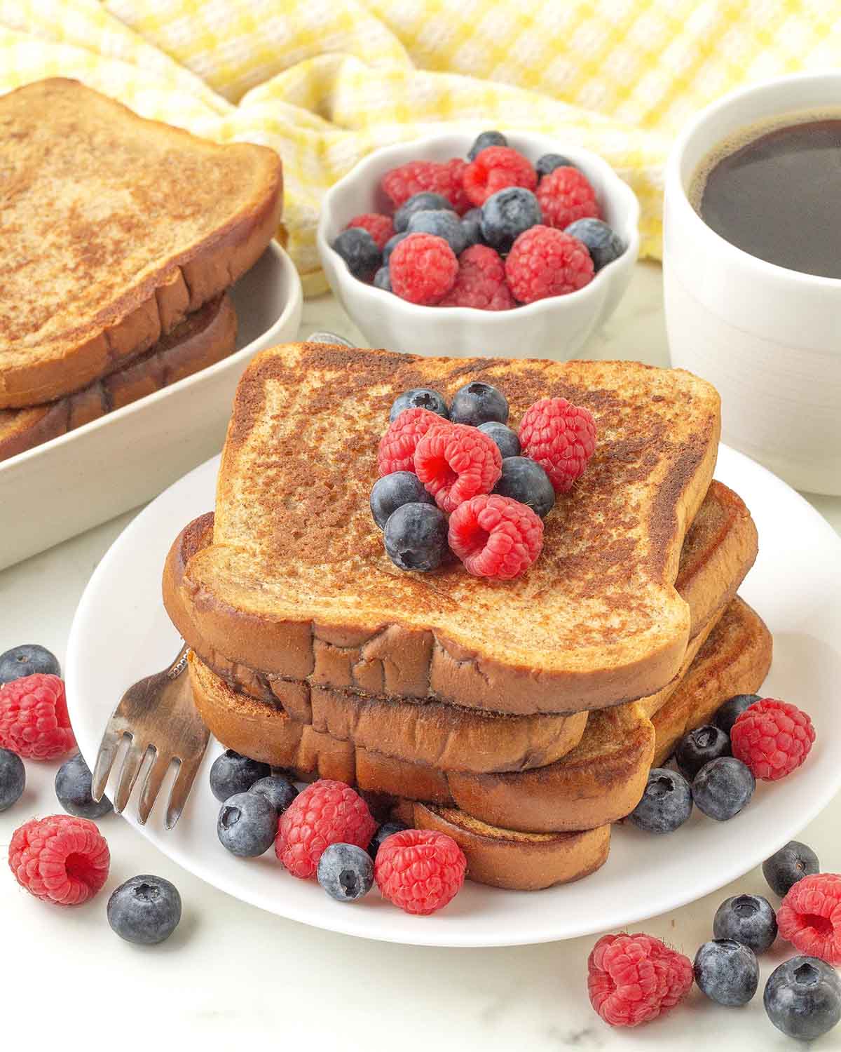 Four pieces of French Toast on a plate with fresh berries and a fork.