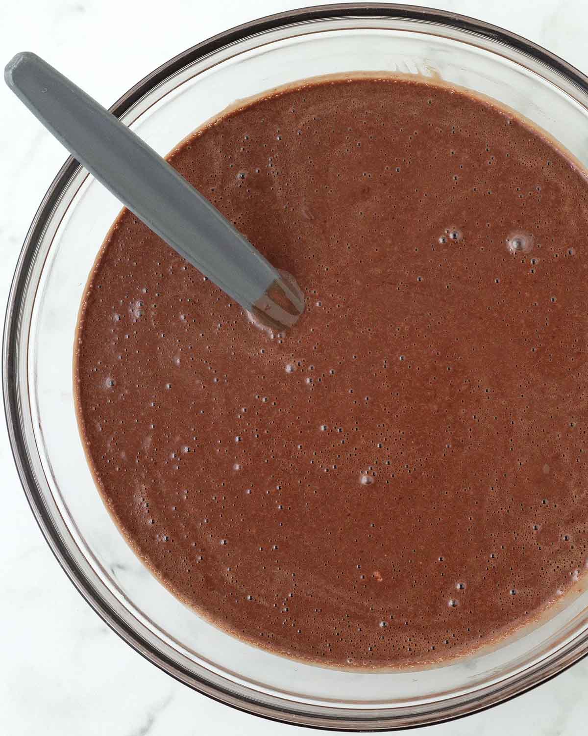 Mixed chocolate sheet cake batter in a glass bowl with a mixing spatula.