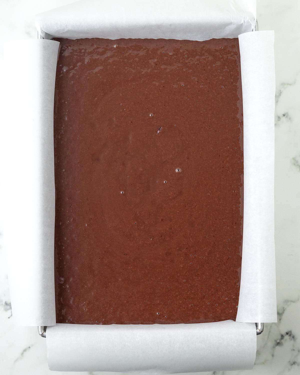 Unbaked chocolate sheet cake batter in a rectangle, parchment lined baking pan.