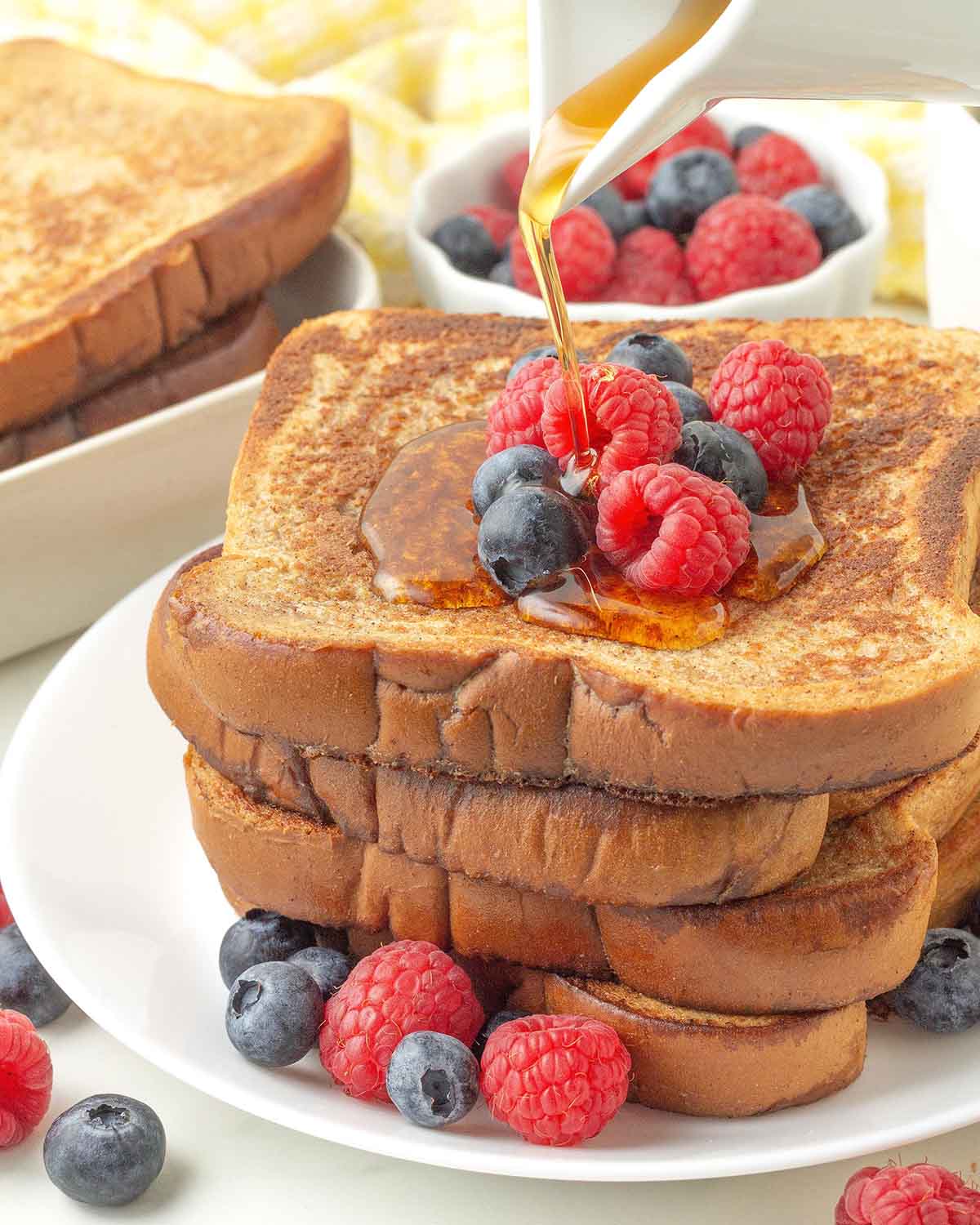 Maple syrup being poured onto a stack of French toast.