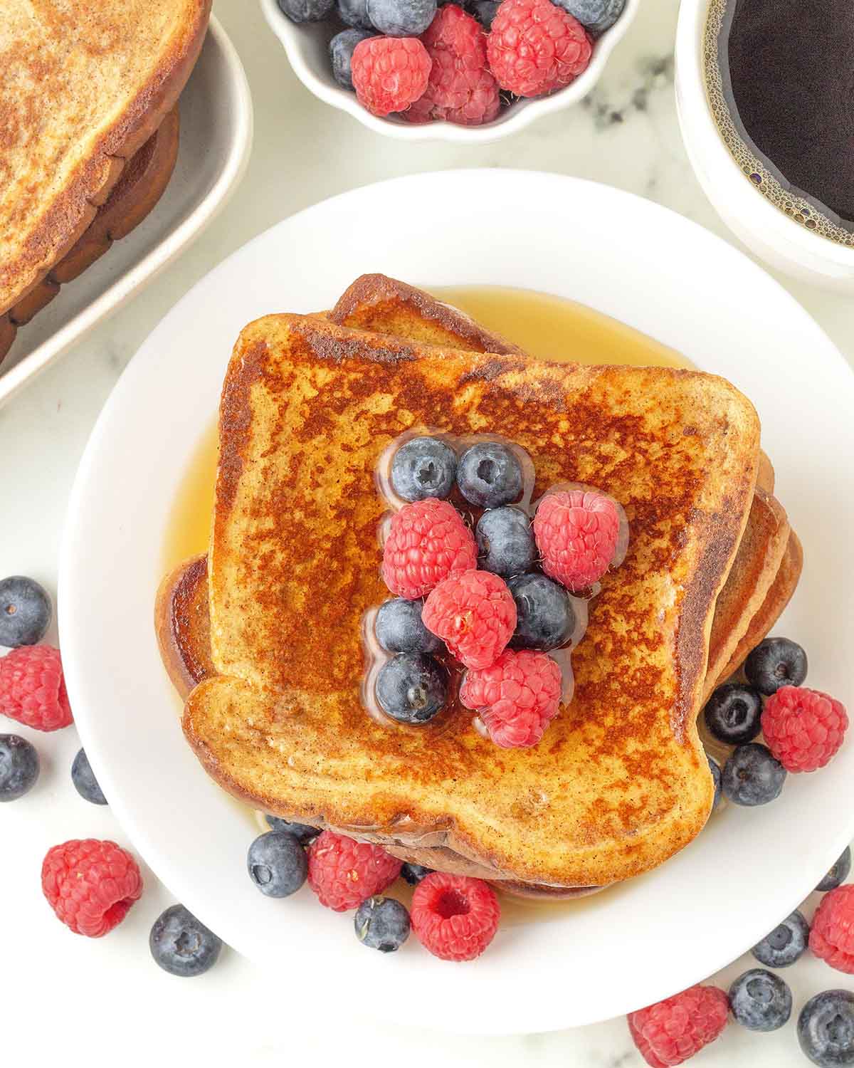 An overhead image of French toast on a plate with berries and syrup on top.