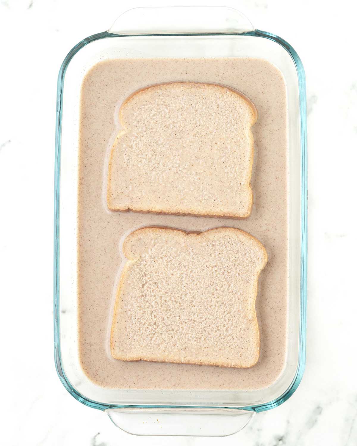 Two pieces of French toast soaking in the milk mixture before frying.