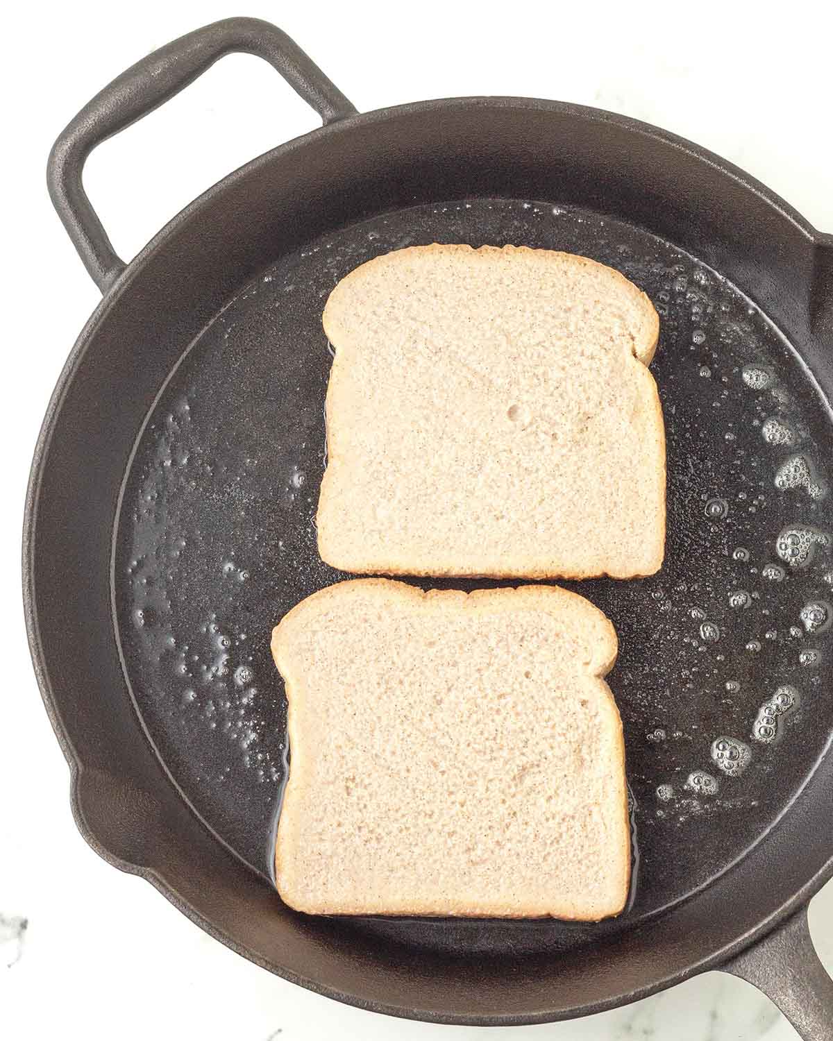 Two pieces of uncooked French toast just added to a cast iron skillet.