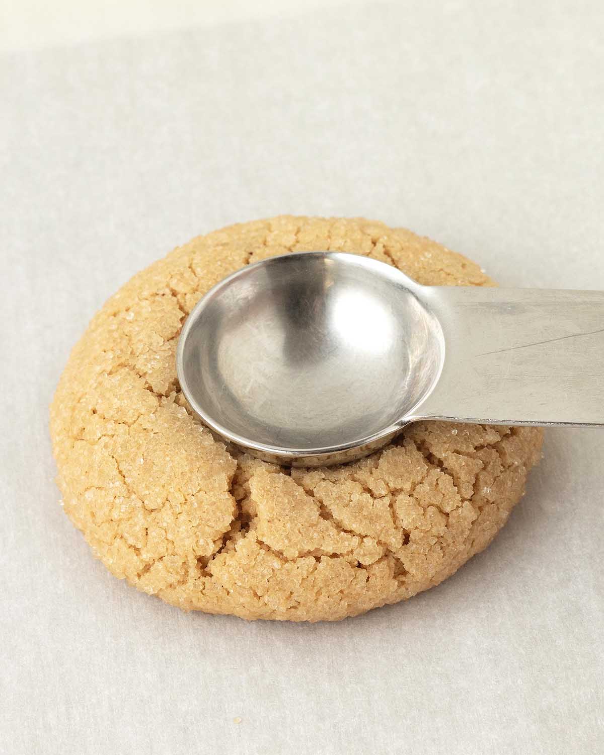 A measuring spoon being pressed into a baked cookie to create an indent for filling.