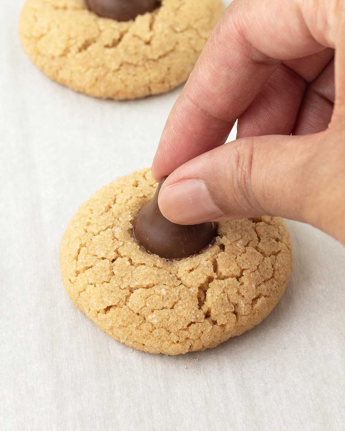 A hand pressing a chocolate kiss into a peanut butter cookie.