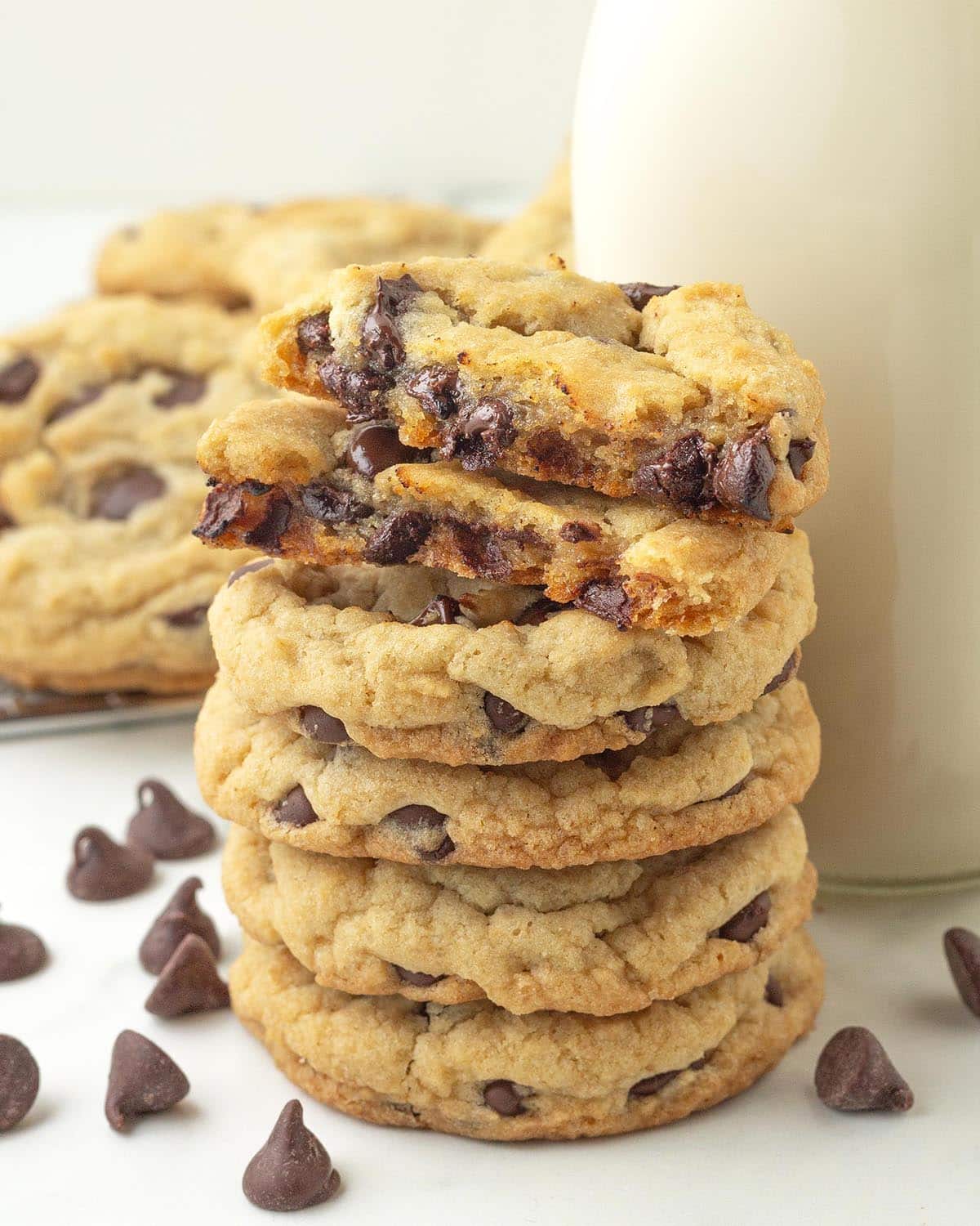 A stack of five chocolate chip cookies, the one on top has been split in two to show the soft, gooey inner texture.