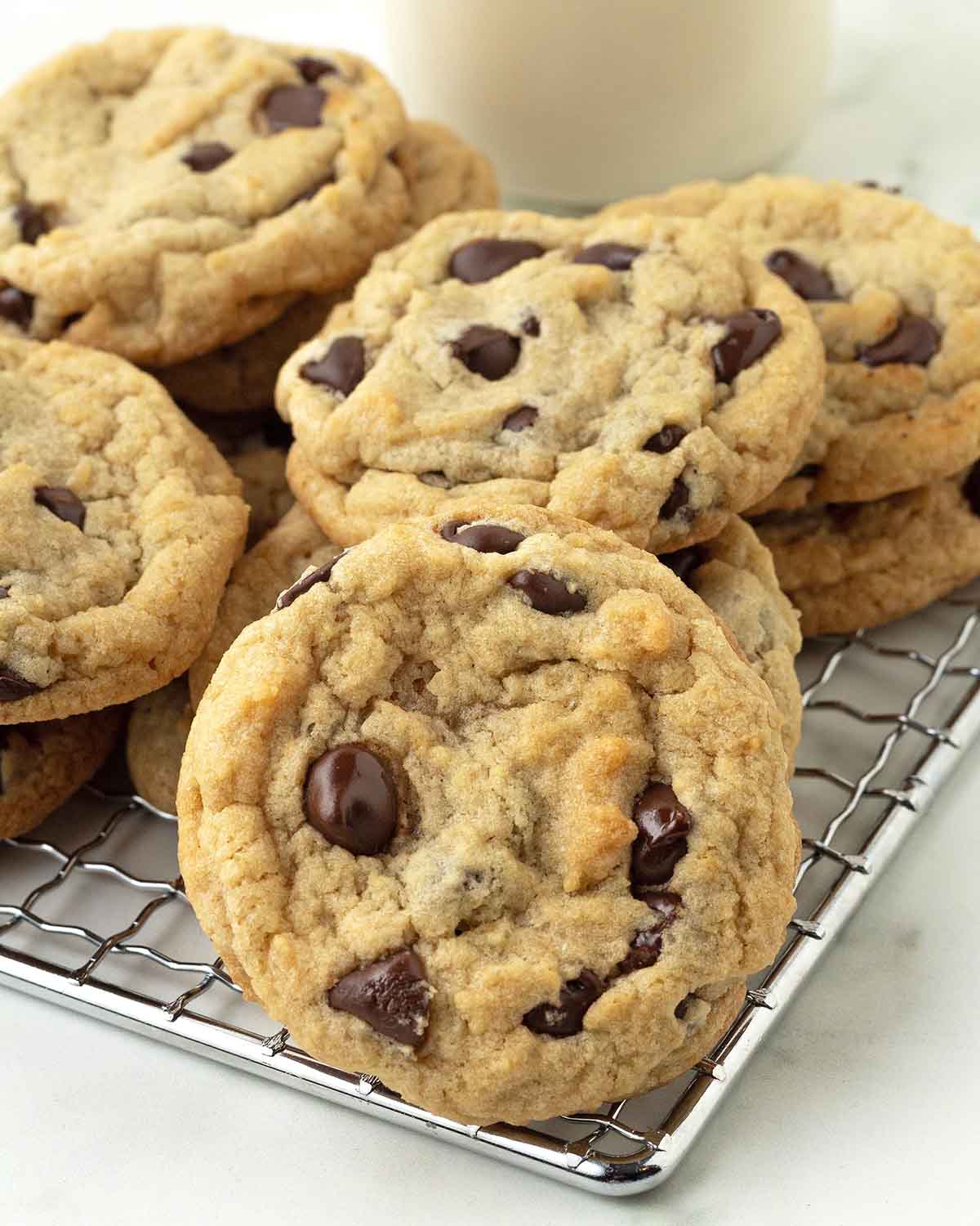 Vegan chocolate chip cookies on a metal rack, the one in the front is propped up against the others.