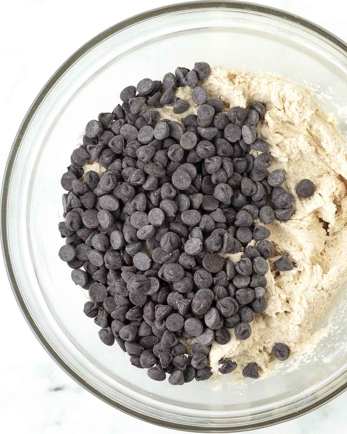 Cookie dough in a bowl with chocolate chips on top waiting to be stirred in.