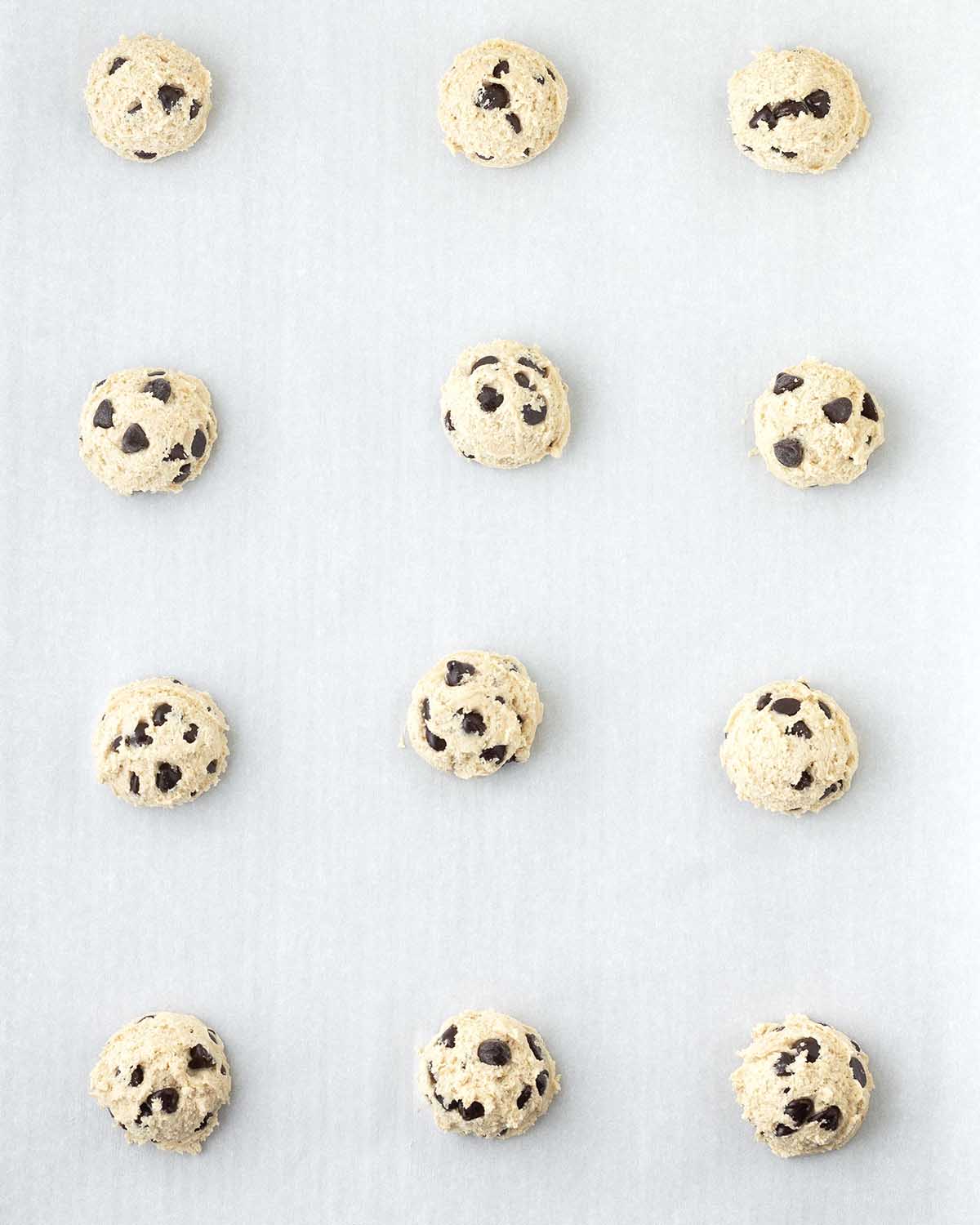 Raw chocolate chip cookie dough balls on a cookie sheet.