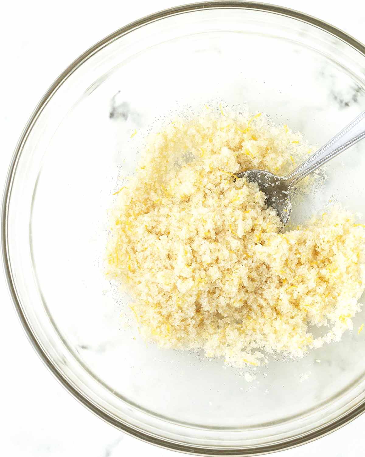 Lemon zest, sugar and a spoon in a glass bowl.