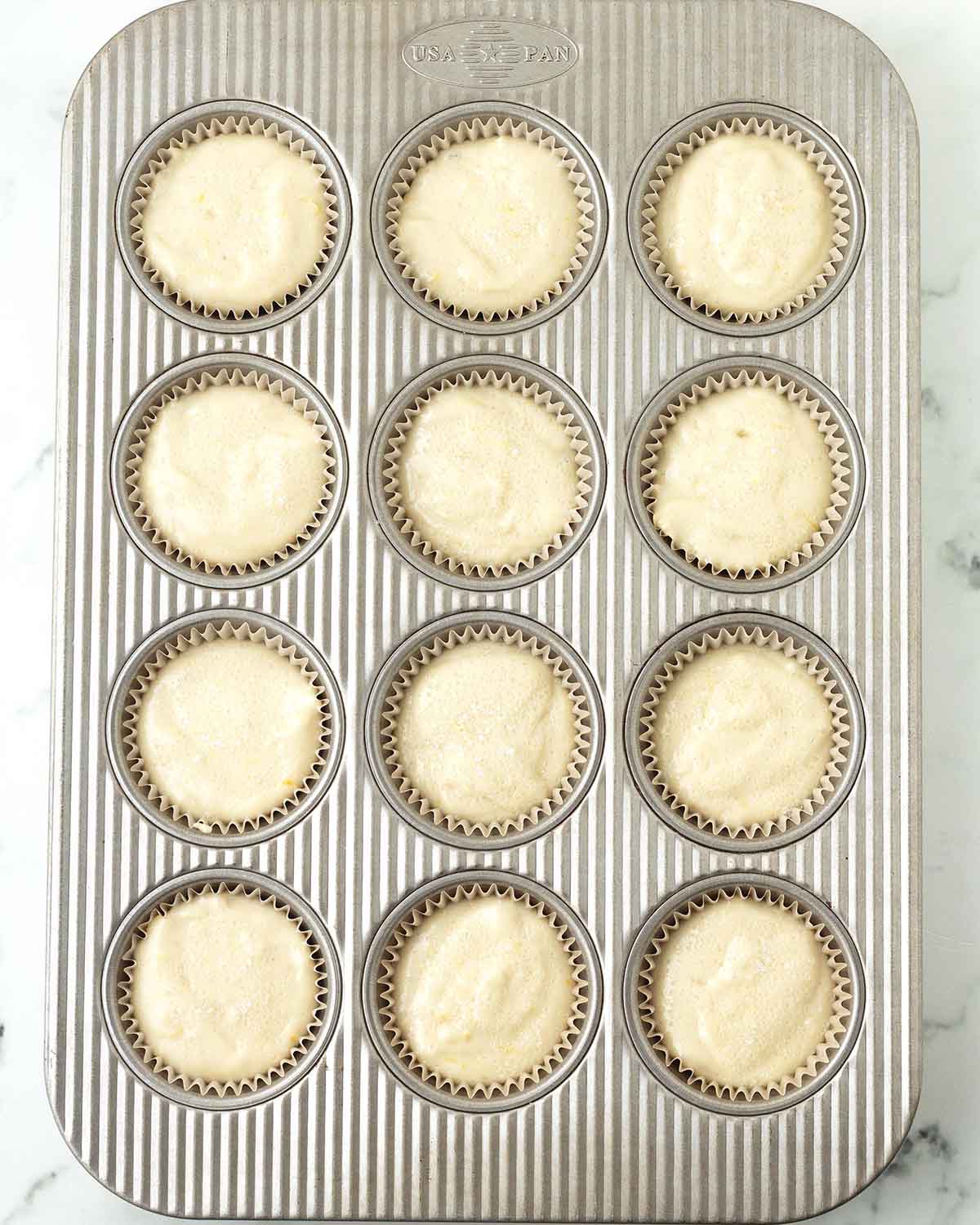 Unbaked lemon muffins in a muffin pan.