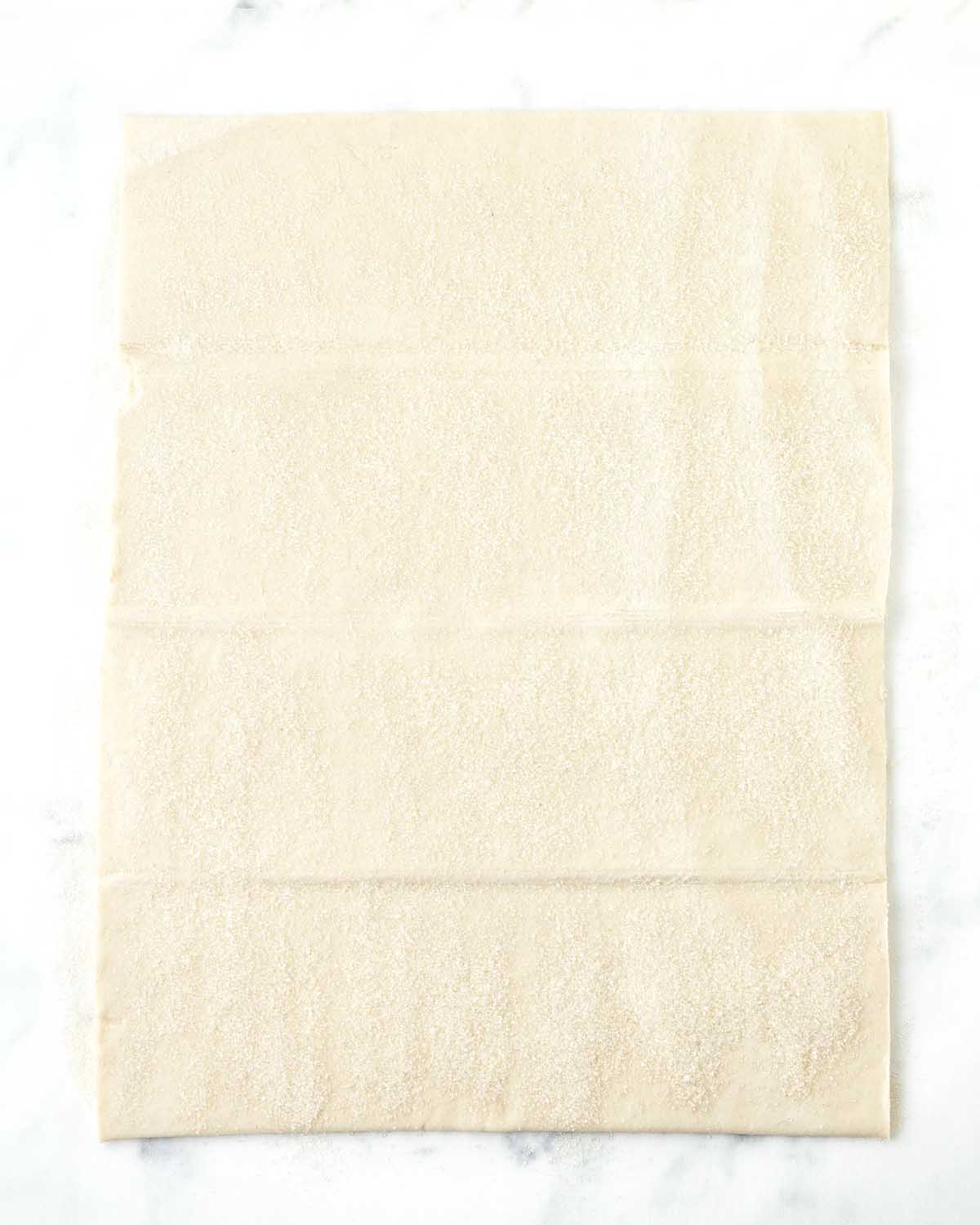 A sheet of puff pastry with sugar sprinkled on top.