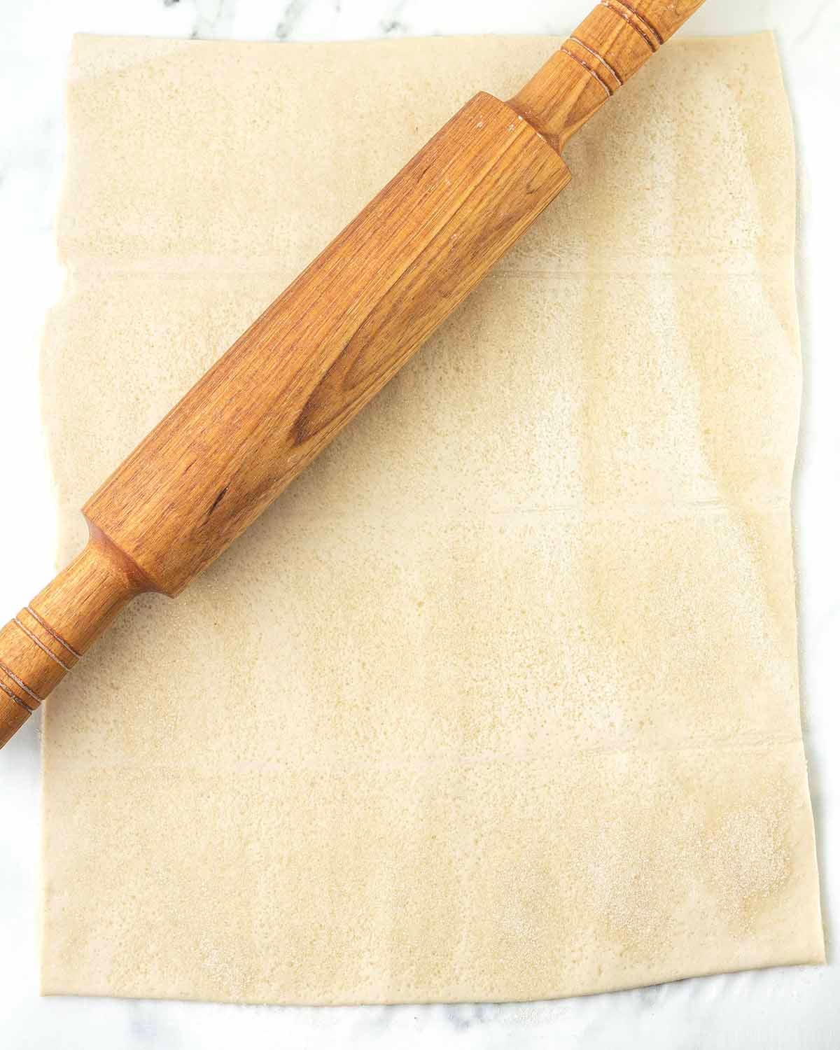 A rolled and sugared sheet of puff pastry, a rolling pin sits on the pastry.