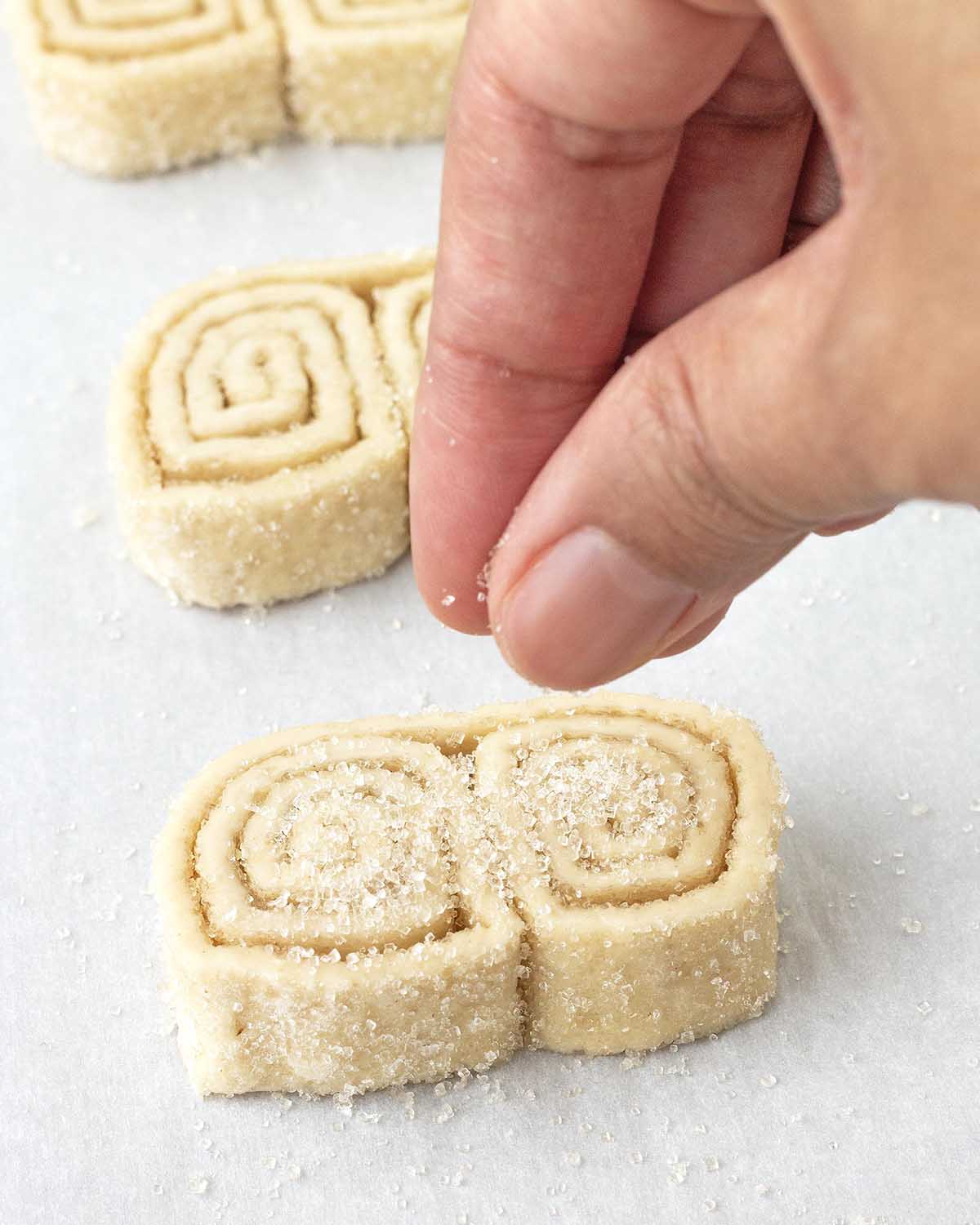 A hand sprinkling sugar onto an unbaked vegan palmier.