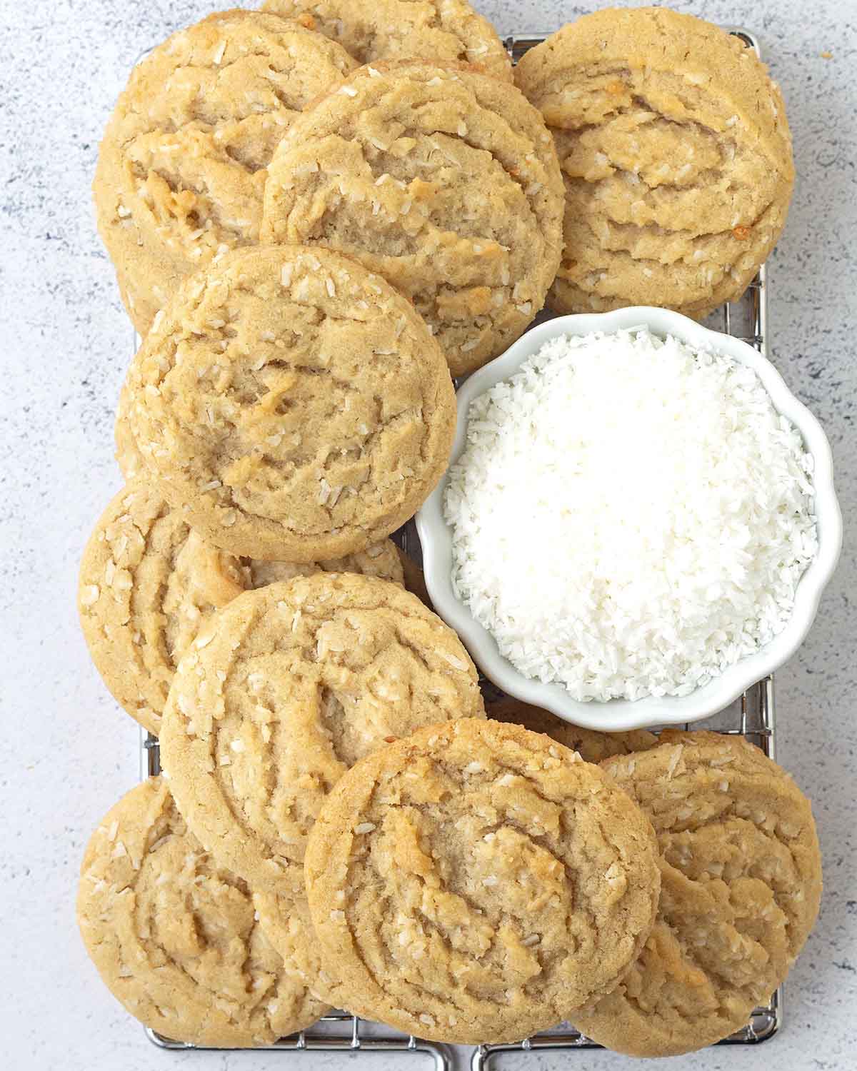 Coconut cookies and a small bowl of shredded coconut on a metal rack.
