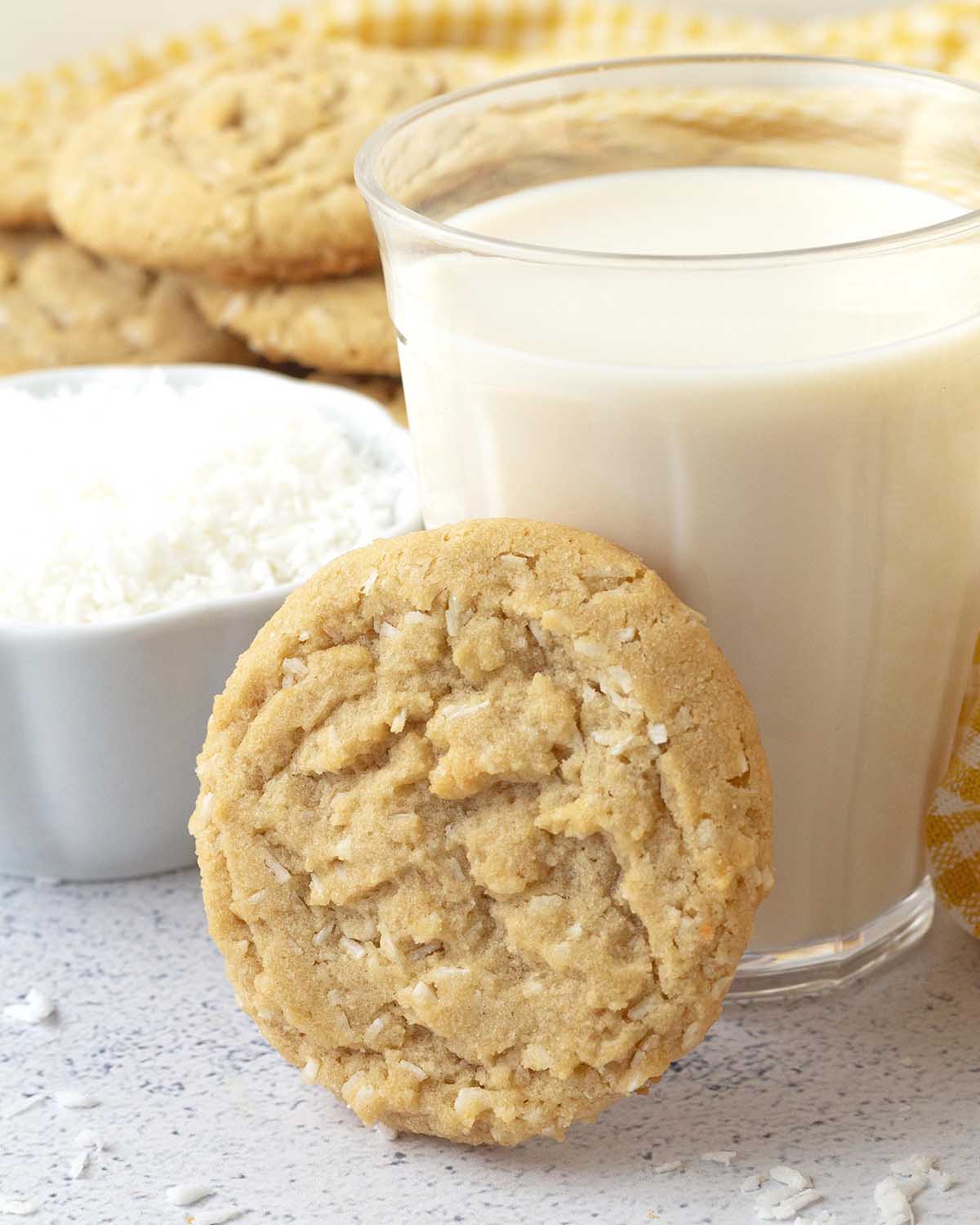 A vegan coconut cookie leaning against a glass of soy milk.